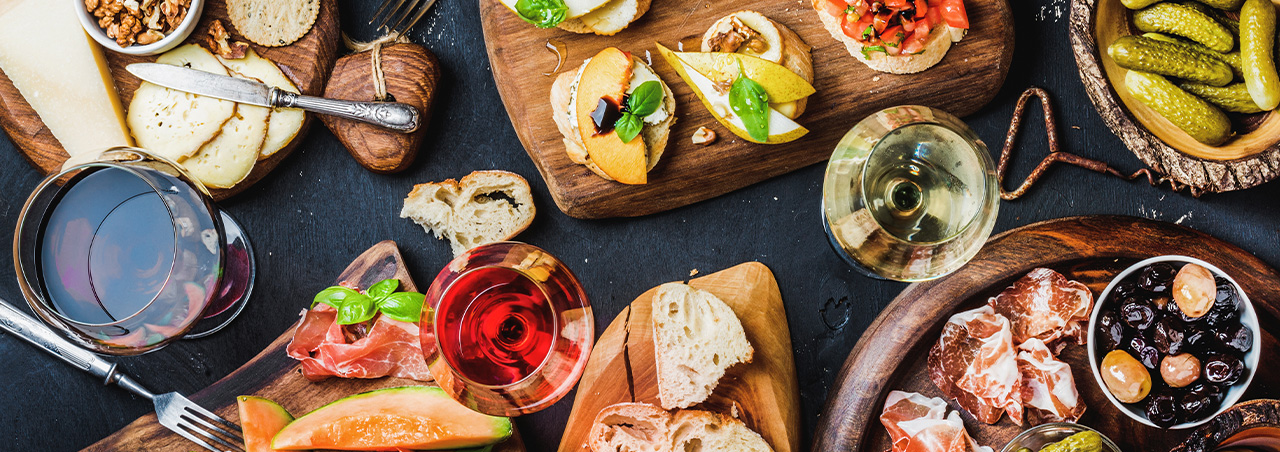 Ansprechende Antipasti, Vorspeisen und Weine auf einer dunklen Tischplatte