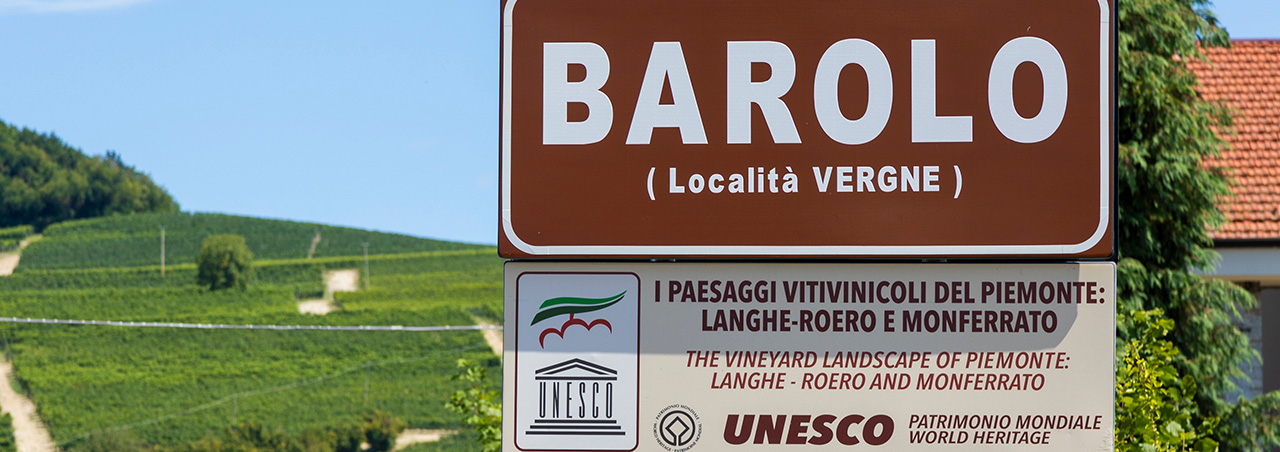 Barolo-Schild mit UNESCO-Siegel, im Hintergrund Weinberg mit Reben