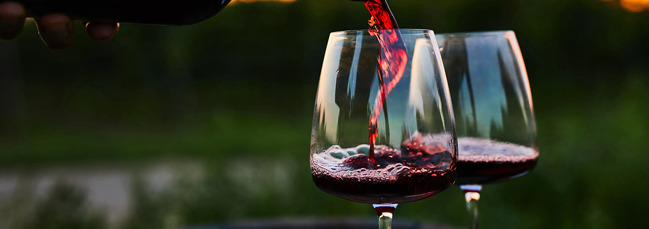 Rotwein wird in der Abenddämmerung in Gläser auf altem Barrique einschenkt