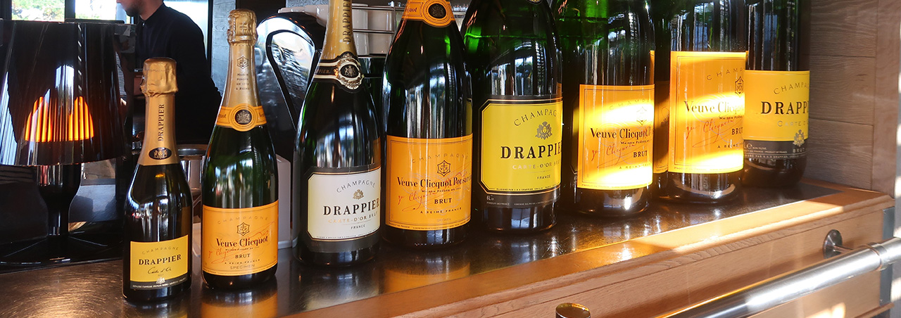 Acht Champagner-Flaschen von den Marken Champagne Veuve Cliquot und Drappier auf einem Bar-Tresen, angeordnet nach Flaschengrösse