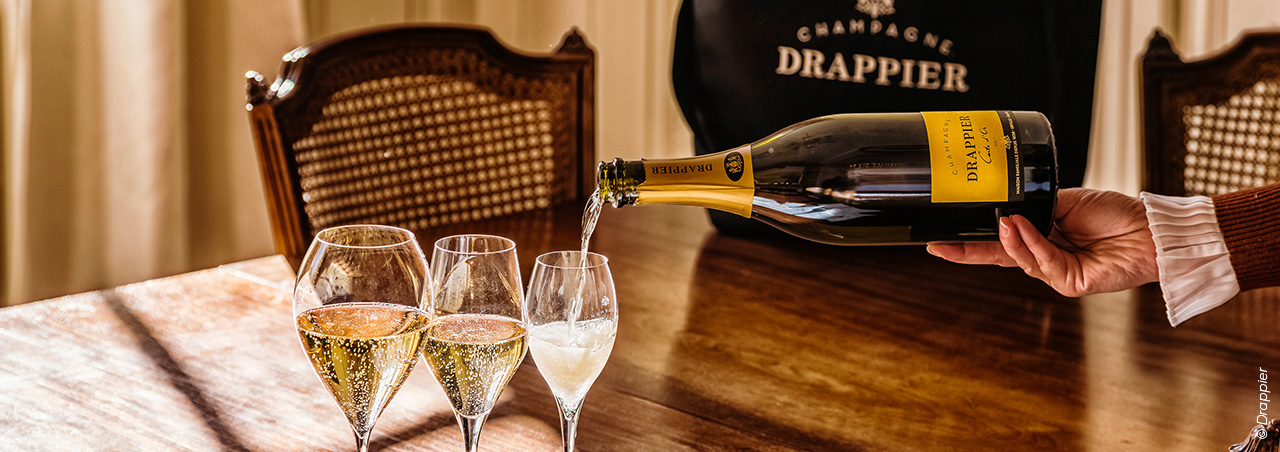 © Drappier, 3 Champagnergläser auf Holztisch werden mit Drappier-Champagner gefüllt