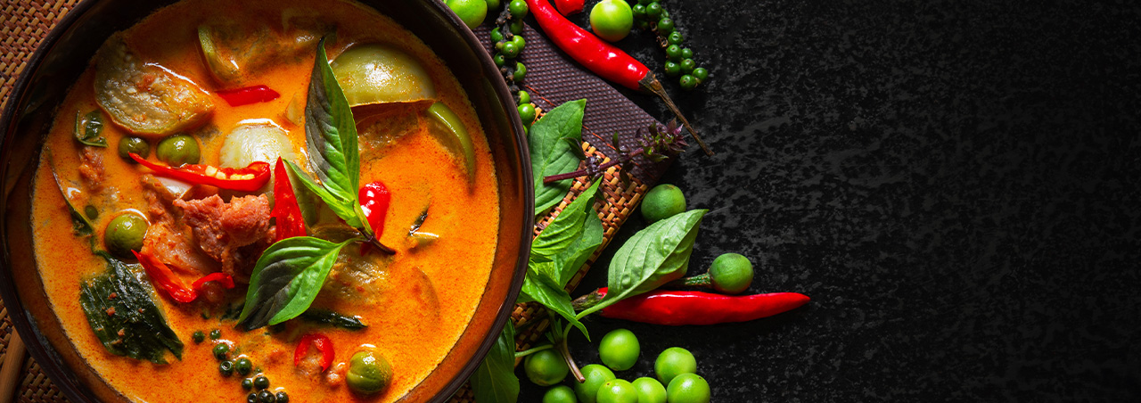 Traditionelles rotes Thai-Curry, mit Basilikum dekoriert. Im Hintergrund Erbsten
