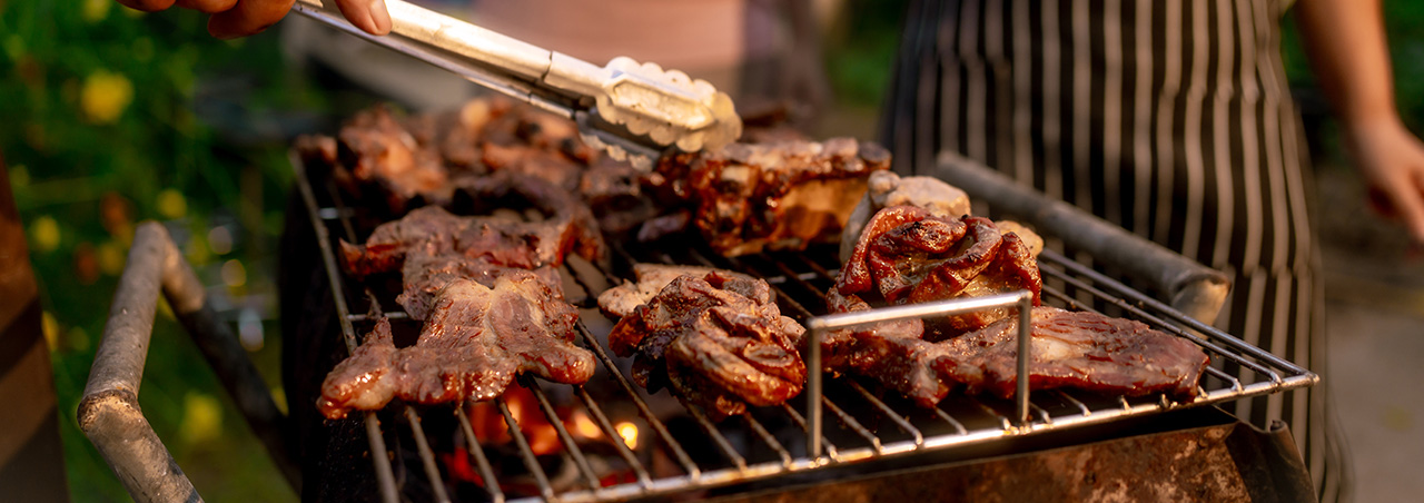 Fleisch wird auf Grillparty gegrillt, im Hintergrund wird mit Rotwein angestossen