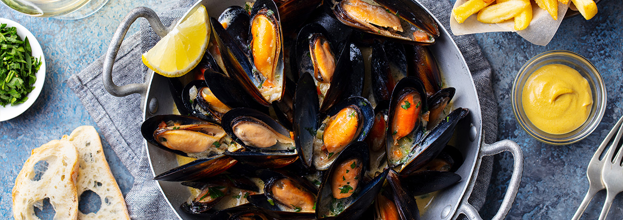 Moules-frites Aufnahme von oben auf blau-grauer Tischdecke. Dazu Brot und goldene Pommes-frites