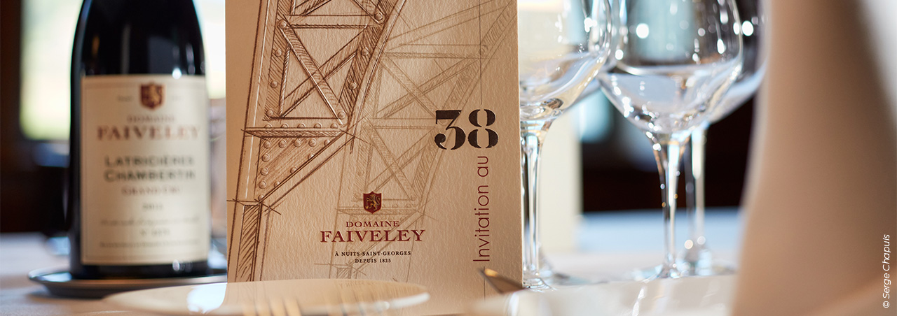 Une photographie mettant à l'honneur un vin de la Maison Faiveley, présenté aux côtés d'un coffret et de verres délicats.