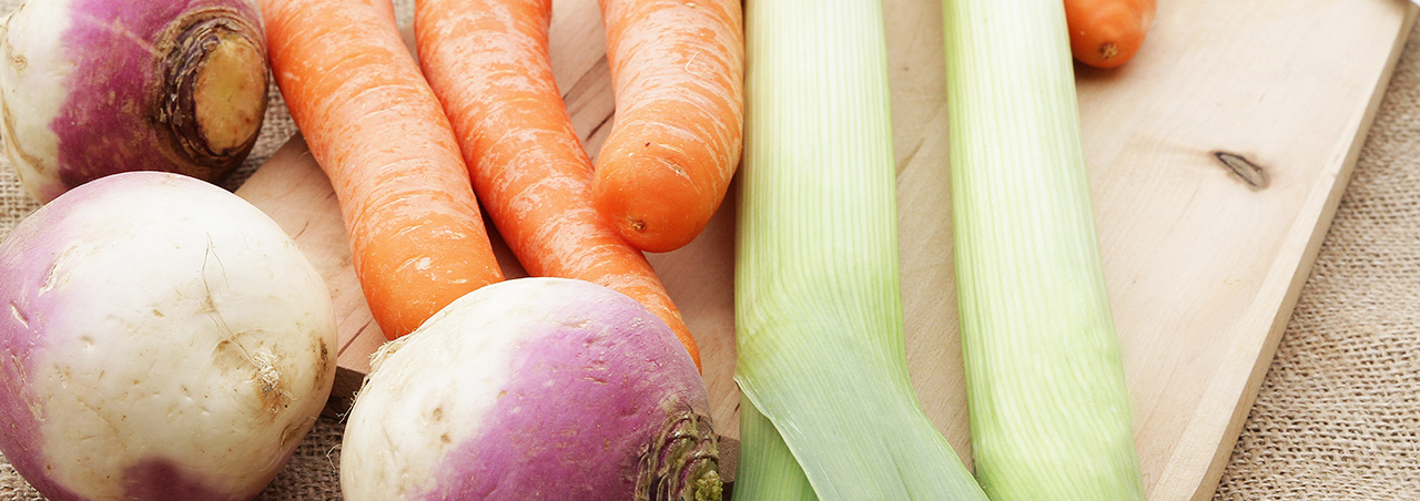 Une photographie de légumes disposés sur un établi, destinés à composer le pot-au-feu : carottes, navets et poireaux.