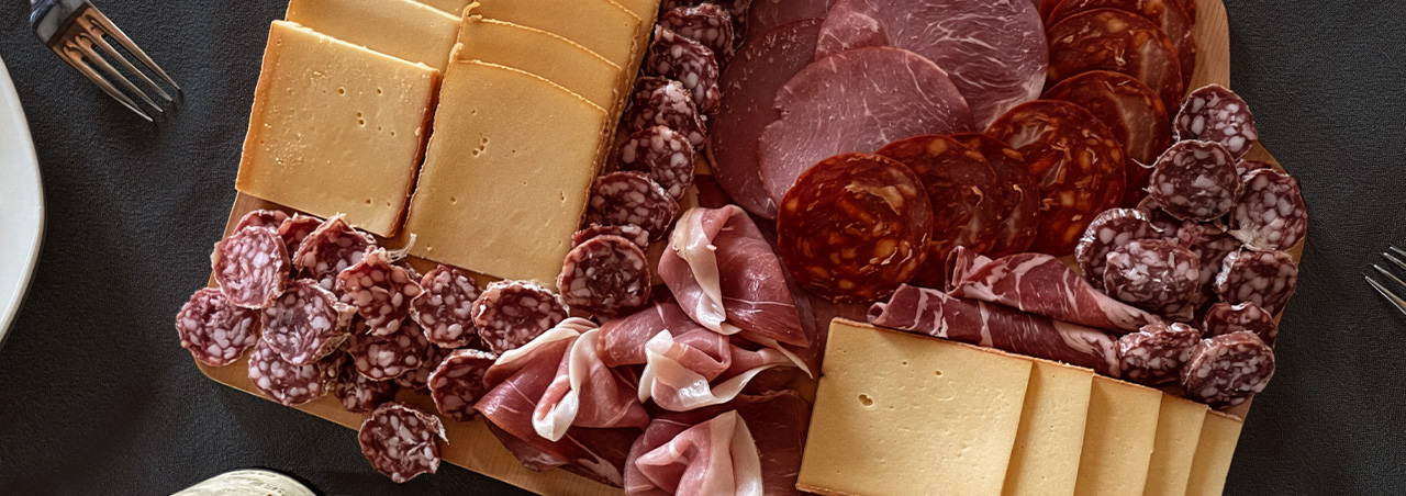Un assortiment de fromage à raclette disposé sur un plateau, sublimé par une sélection de charcuterie fine.