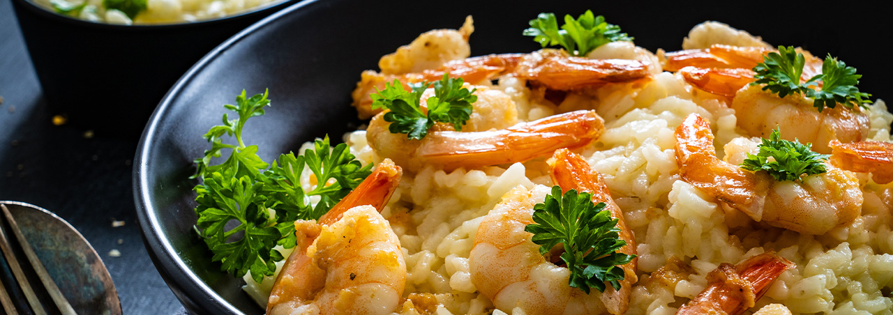 Une photo raffinée d'un risotto crémeux aux crevettes, parsemé d'herbes aromatiques fraîches, présenté avec soin dans un plat élégant. 