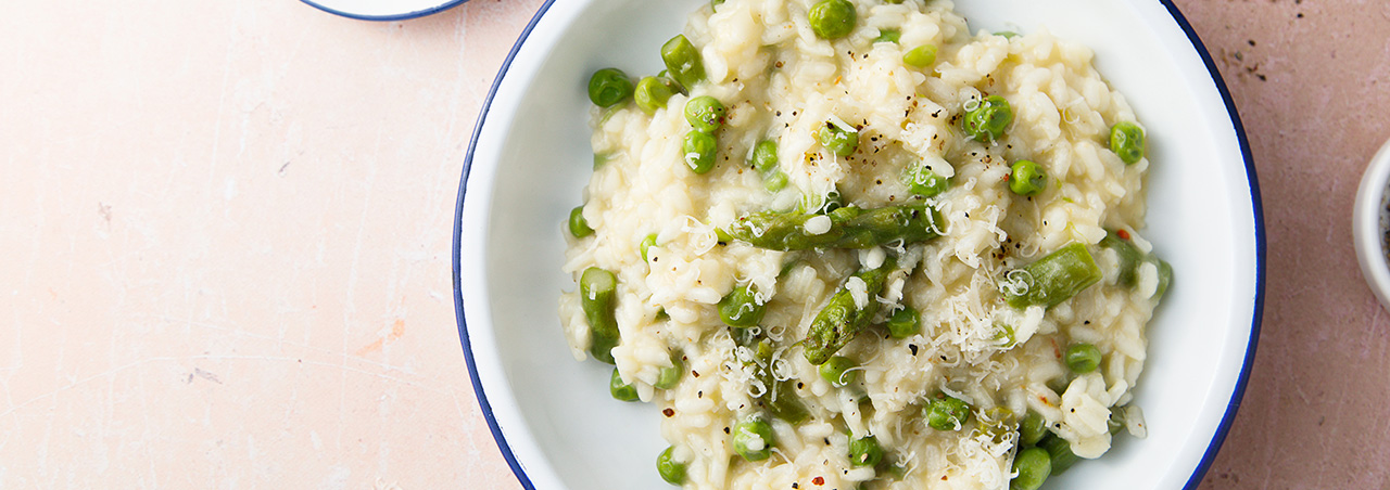 Une photo d'un plat de risotto aux asperges, parsemé de copeaux de parmesan.