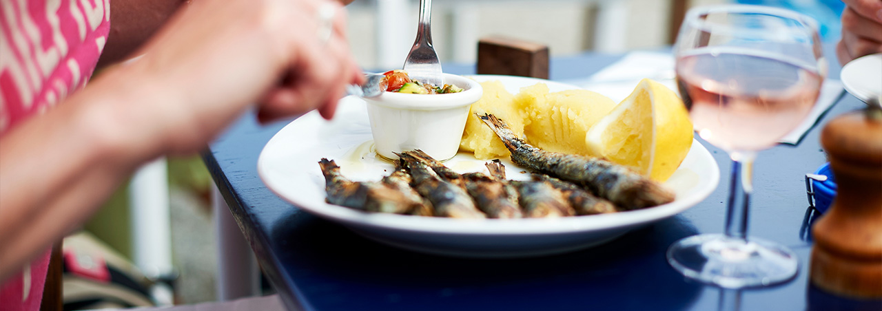 Gegrillte Sardinen mit Zitronenscheiben in rundem Teller, daneben ein Glas Rosé