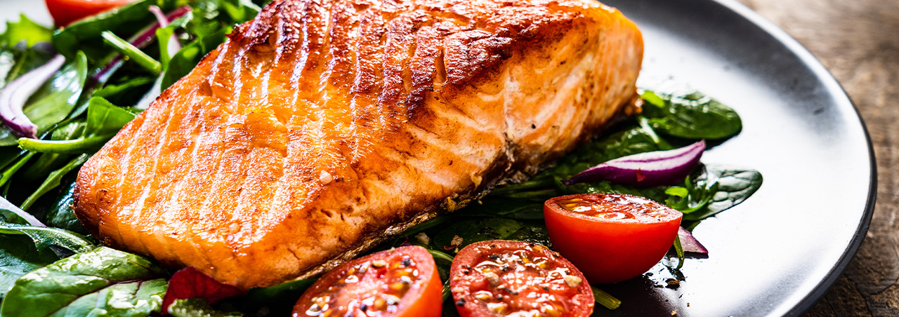 Gegrilltes Lachsfilet auf Salatbett und Cocktail-Tomaten, serviert in schwarzem Teller auf Holztisch