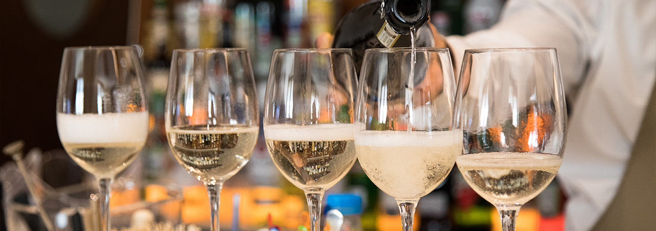 Nahaufnahme von vier gefüllten Prosecco-Gläsern auf einem Bar-Tresen