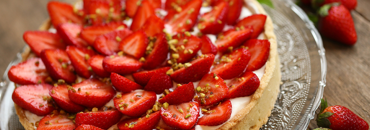 Nahaufnahme von Erdbeer-Tarte auf rundem Glasteller, im Hintergrund Minzblätter
