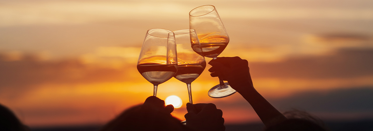 Anstossen mit drei Weingläsern vor Sonnenuntergang