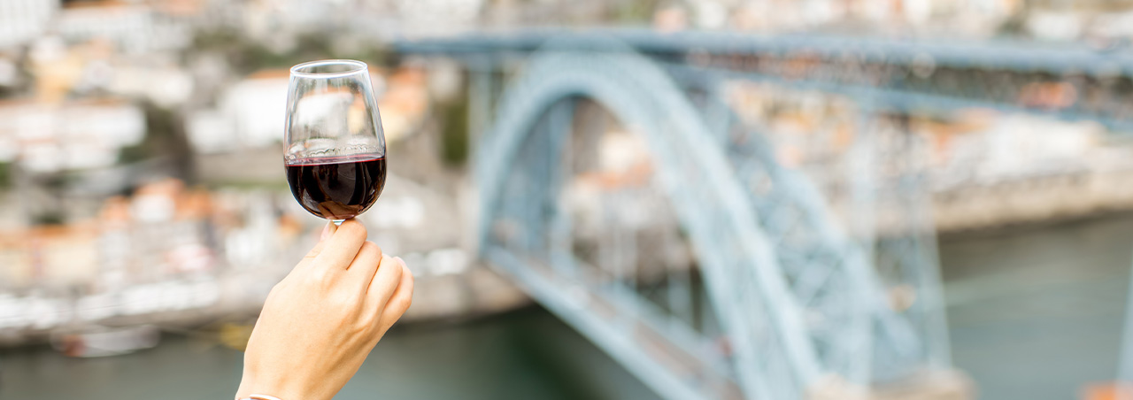 Eine Frau hält ein gepflegtes Glas Rotwein in die Luft. Im HIntergrund die Stadt Porto und der Duero-Fluss