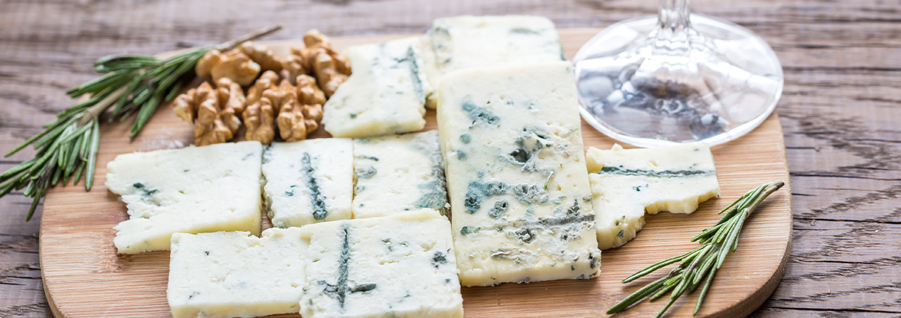 Roquefort-Käse auf Holzbrett, dazu ein Glas Süßwein im Sauternes-Stil, Walnüsse und Kräuter
