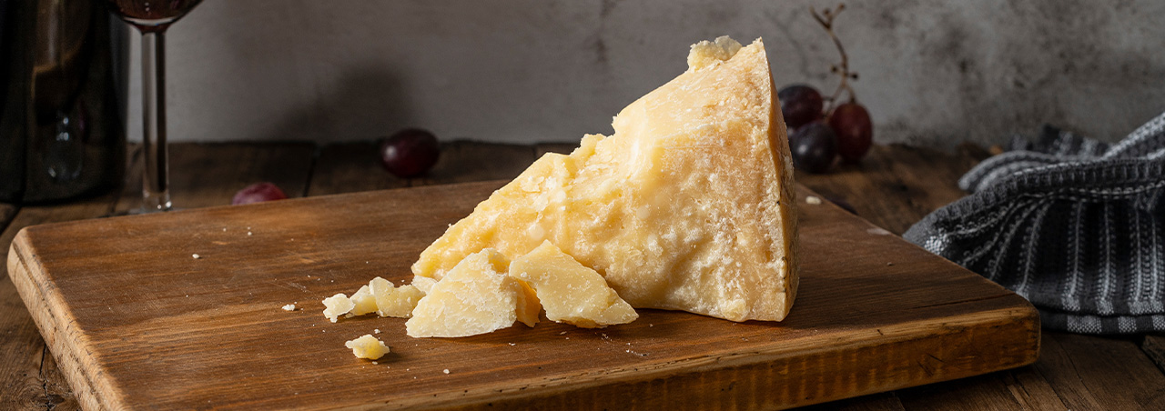 Elegant präsentierter Parmesan Käse auf Holzbrett, im Hintergrund ein Glas Rotwein