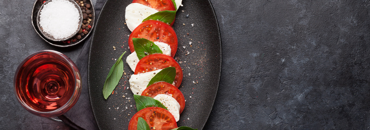 Italienischer Caprese-Salat mit Tomate, Mozzarella und Basilikum, dazu ein Glas Roséwein auf Schieferplatte