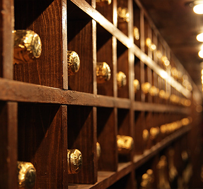 Seitenansicht von Weinregalen aus Holz mit liegenden Champagnerflaschen in dunklem Weinkeller