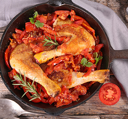Une photographie d'un plat de poulet basquaise, mettant en avant une piperade savoureuse et un poulet rôti dressés harmonieusement dans un même plat.