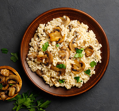 Une photo d'un plat de risotto aux champignons, parsemé de copeaux de parmesan et d'herbes aromatiques.
