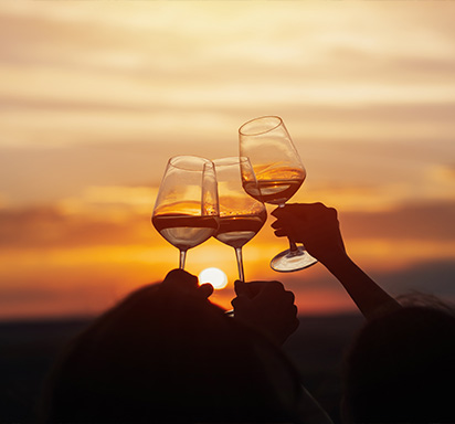 Anstossen mit drei Weingläsern vor Sonnenuntergang