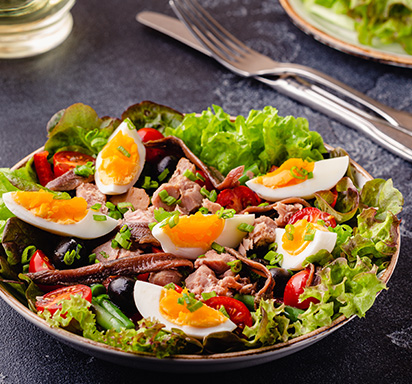 Salade Niçoise auf Schieferplatte; geviertelte Eier, Kirschtomaten Thunfisch und Anchovis auf Salatbett