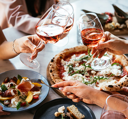 Freunde genießen eine Dinnerparty mit Pizza und Roséwein in einer Bar oder einem Restaurant