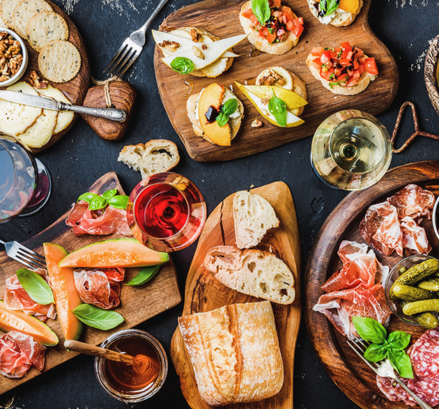 Ansprechende Antipasti, Vorspeisen und Weine auf einer dunklen Tischplatte