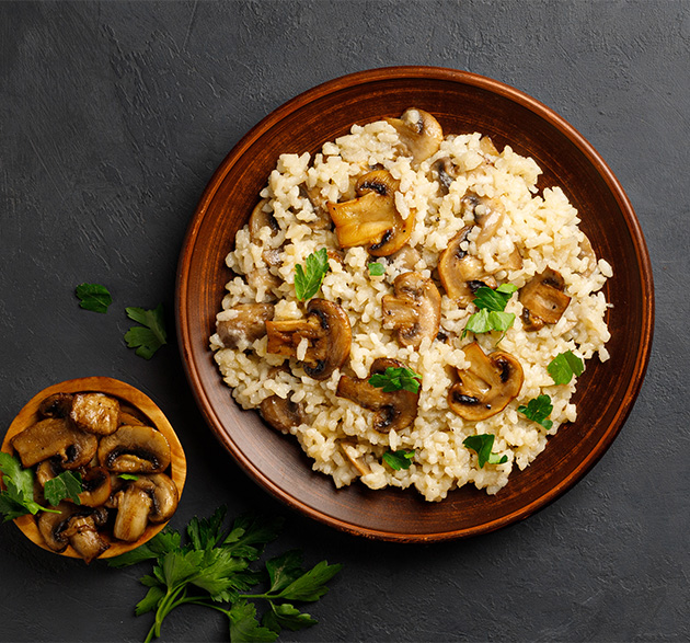 Une photo d'un plat de risotto aux champignons, parsemé de copeaux de parmesan et d'herbes aromatiques.