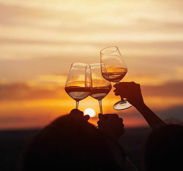Anstossen mit drei Weingläsern vor Sonnenuntergang