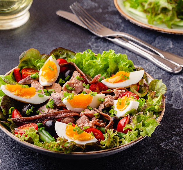 Salade Niçoise auf Schieferplatte; geviertelte Eier, Kirschtomaten Thunfisch und Anchovis auf Salatbett; welcher Wein harmoniert?