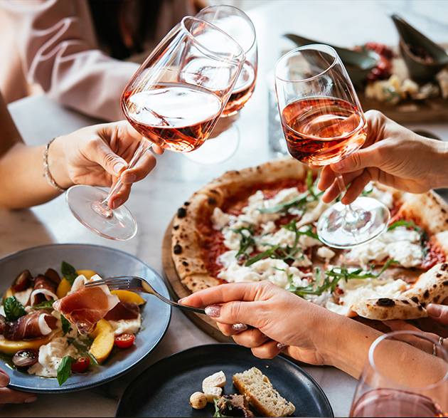 Freunde genießen eine Dinnerparty mit Pizza und Roséwein in einer Bar oder einem Restaurant
